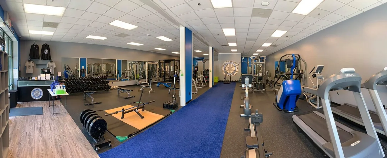 Wide interior view: dumbbell rack, lifting platform, cable stations, and Precor cardio along the back wall.