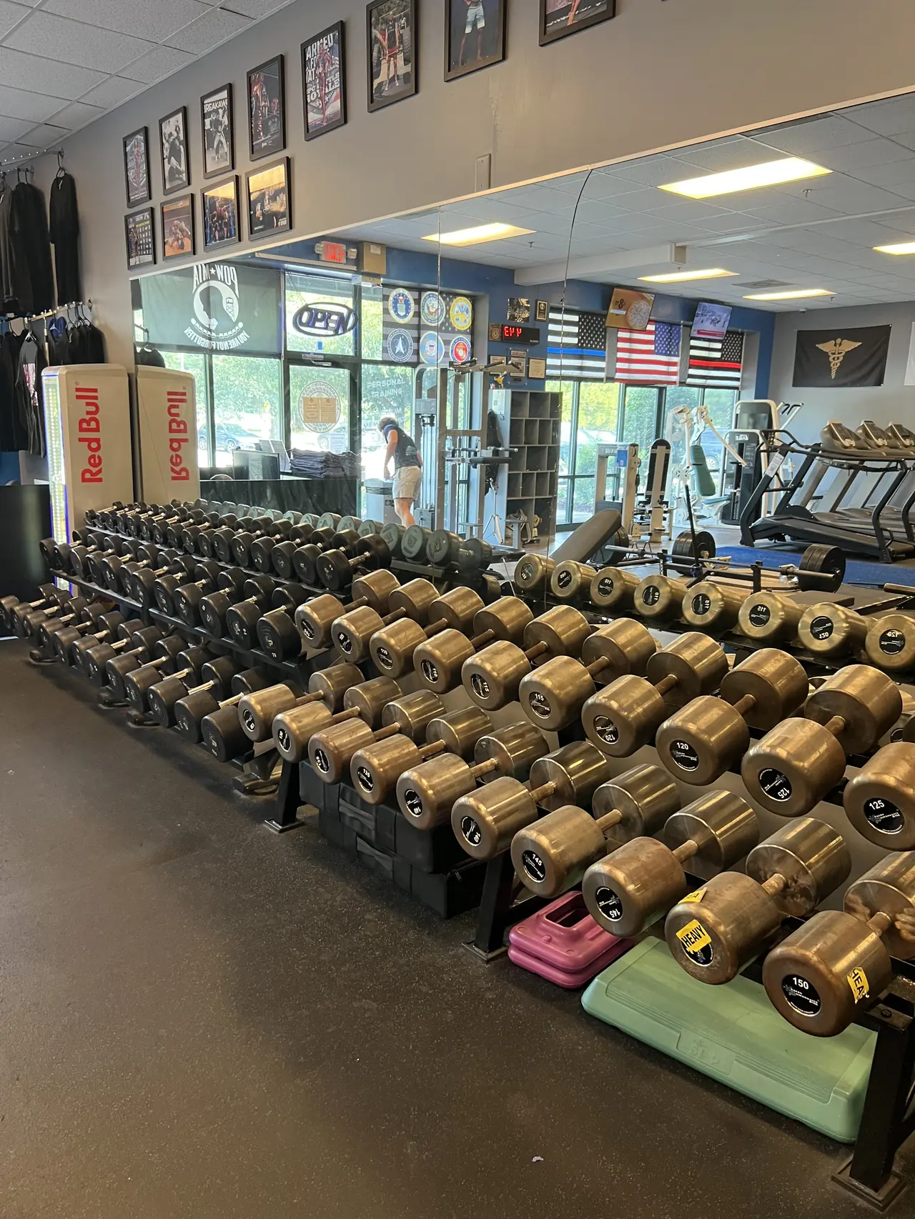 Rows of Intek dumbbells running up to 150 lb, with the front desk and the cardio deck behind.