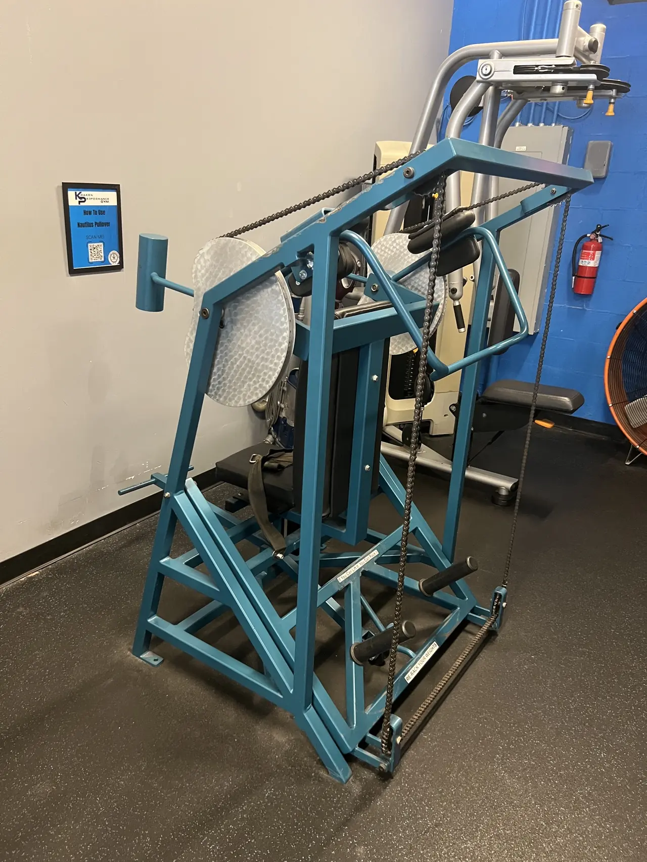 Teal Nautilus pullover machine, with a scan-to-learn how-to-use card on the wall.