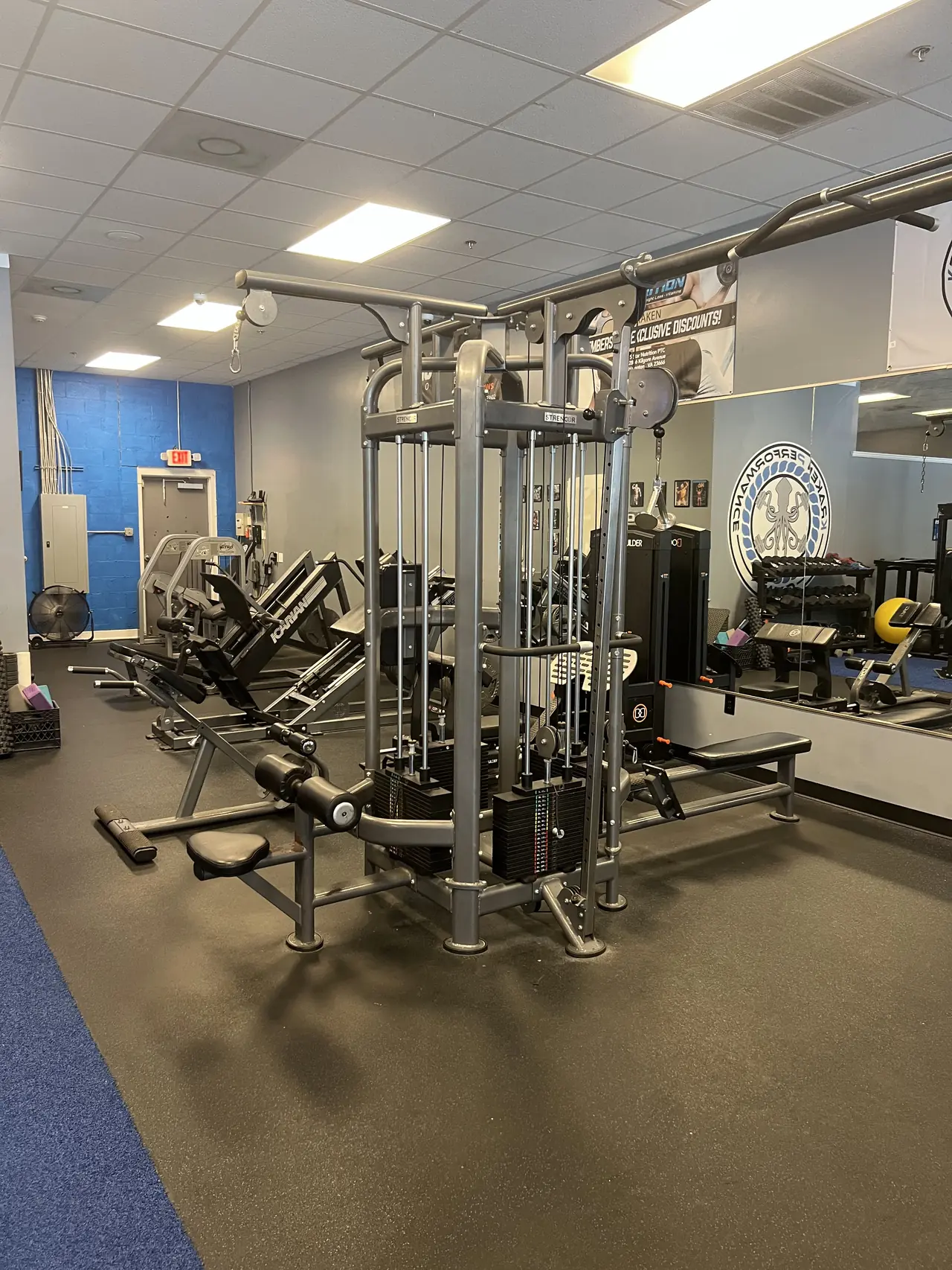 Four-stack cable jungle gym mid-floor, leg machines and the mirrored logo wall behind.