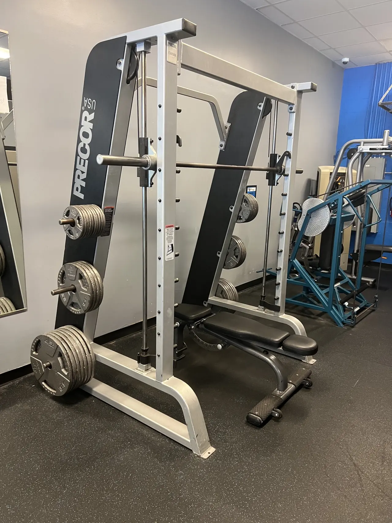 Precor Smith machine with plate horns loaded and an adjustable bench underneath.